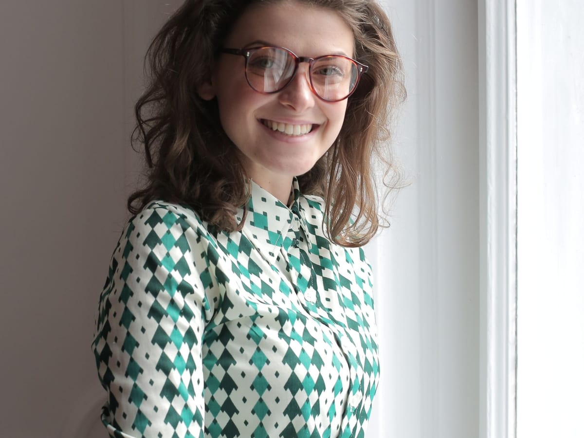 Lächelnde Frau mit Brille am Fenster einer Wohnung