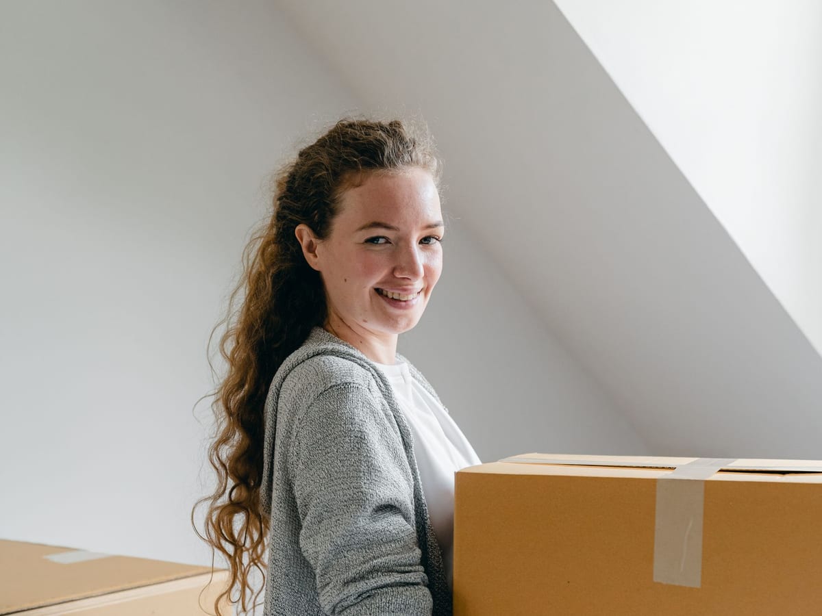 Frau trägt lächelnd Umzugskartons in ihr neues Zuhause
